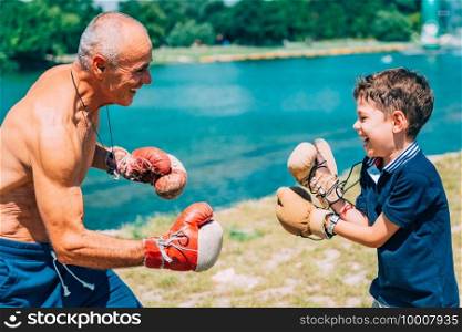 Little boy practicing boxing with grandfather by the lake