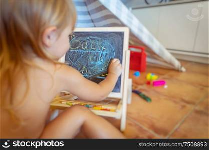 Little boy preparing for school, cute kid writing words on the chalkboard in his playroom at home, the child plays and learns at the same time, back to school concept