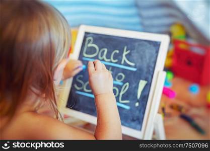 Little boy preparing for school, sweet adorable child writing words on the chalkboard in his playroom at home, back to school concept