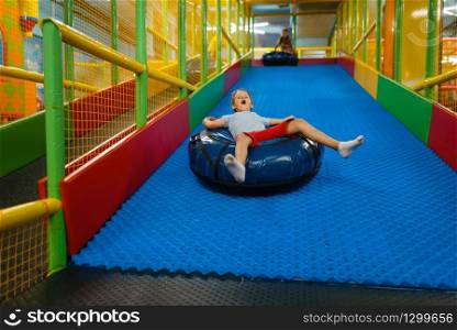 Little boy rides on tubing, playground in entertainment center. Play area indoors, playroom