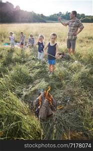 Little boy roasting marshmallow over a campfire. Family spending time together on a meadow, close to nature. Parents and children sitting on a blanket on grass. Candid people, real moments, authentic situations
