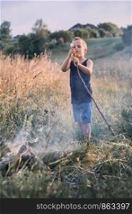 Little boy roasting marshmallow over a campfire on a meadow. Candid people, real moments, authentic situations