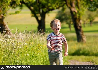 Little boy running down a dirtpath in a beautiful landscape in summer, very light and happy scene