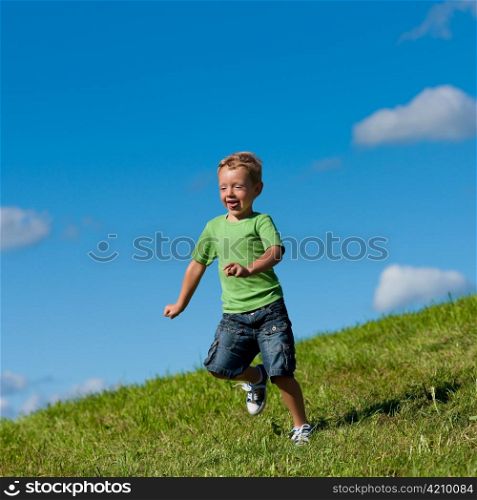 Little boy running down a meadow in a beautiful landscape in summer