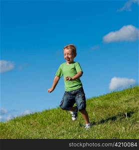 Little boy running down a meadow in a beautiful landscape in summer