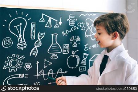 Little boy scientist showing mathematical drawing on blackboard with marker. Side view of boy showing drawing on chalkboard