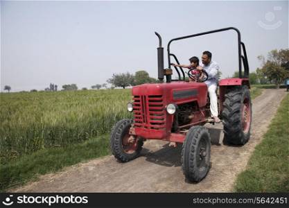 Little boy showing something to father while sitting in tractor