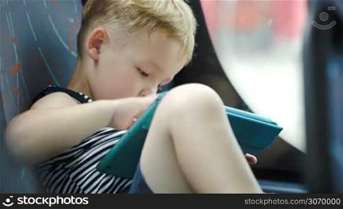 Little boy sitting in car or bus and using touchpad