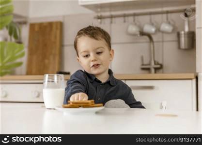 Little boy sitting in the kitchen and drinking milk. Fresh milk in glass, dairy healthy drink. Healthcare, source of calcium, lactose. Cozy and modern interior. Preschool child with casual clothing. Little boy sitting in the kitchen and drinking milk. Fresh milk in glass, dairy healthy drink. Healthcare, source of calcium, lactose. Cozy and modern interior. Preschool child with casual clothing.
