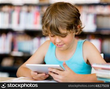 Little boy sitting with tablet in library. Primary school boy with tablet in library