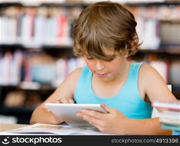Little boy sitting with tablet in library. Primary school boy with tablet in library