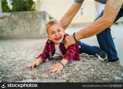 Little boy small child fell on the concrete crying with tears he is hurt senior man father or grandfather is trying to help and lift him up