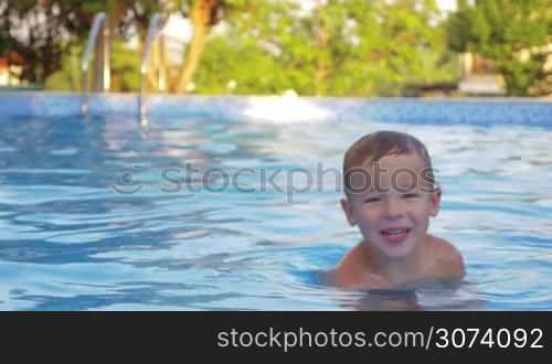 Little boy swimming alone in the outdoor pool. Funny kid enjoying summer vacation