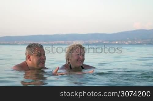 Little boy swimming towards his grandparents. They smiling. Mountains on background.