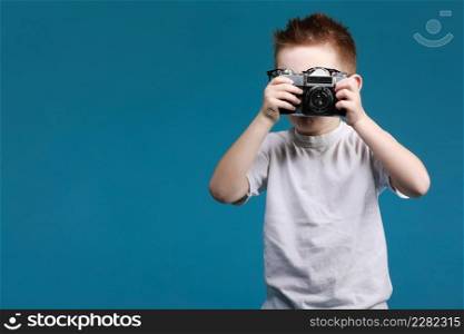 Little boy taking a picture using a retro camera. Child boy with vintage photo camera isolated on blue background. Old technology concept with copy space. Child learning photography .. Little boy taking a picture using a retro camera. Child boy with vintage photo camera isolated on blue background. Old technology concept with copy space. Child learning photography