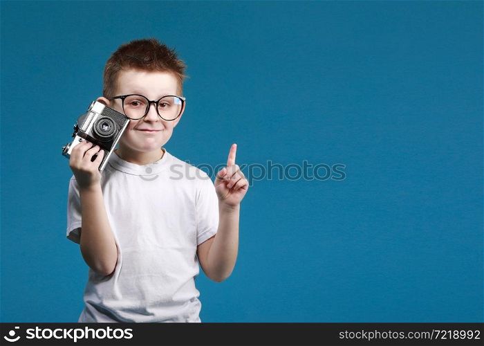 Little boy taking a picture using a retro camera and with finger pointed up. Child boy with vintage photo camera isolated on blue background. Old technology concept. Child learning photography.. Little boy taking a picture using a retro camera and with finger pointed up. Child boy with vintage photo camera isolated on blue background. Old technology concept. Child learning photography