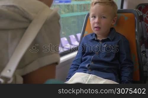Little boy traveling with mother in commuter train, he looking at map on his laps trying to find destination place