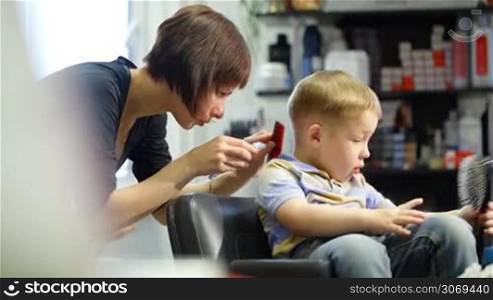 Little boy watching different combs while getting a haircut at the hairdressing saloon