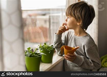 little boy watering plants by window