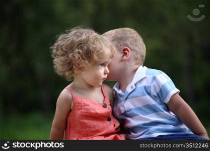 Little boy whispers to lovely girl on ear