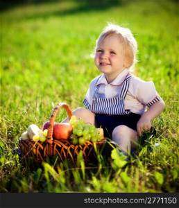little boy with a basket of fruit sits on a grass