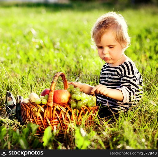 little boy with a basket of fruit sits on a grass