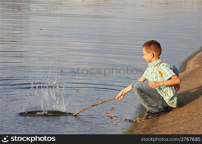 little boy with backpack near pond. he is wallop water. splash.