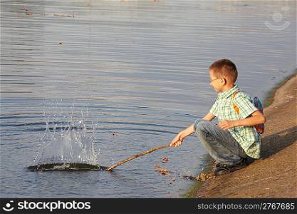little boy with backpack near pond. he is wallop water. splash.