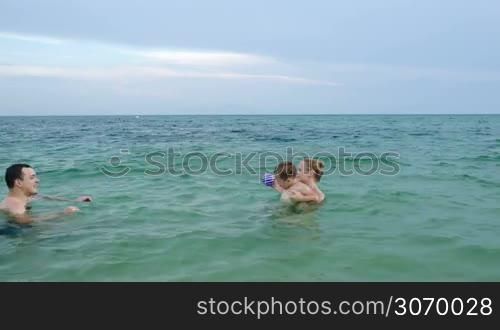 Little boy with ball making his own way in sea water walking from mother to father