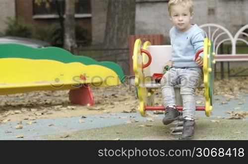 Little boy with his toy tractor going on the swings, then taking something from the ground and moving away leaving his toy on the swing.