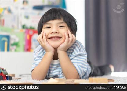 little boy with toothy smile looking at camera. Lovely child lying on front in bedroom. Happy young cute boy lying on floor