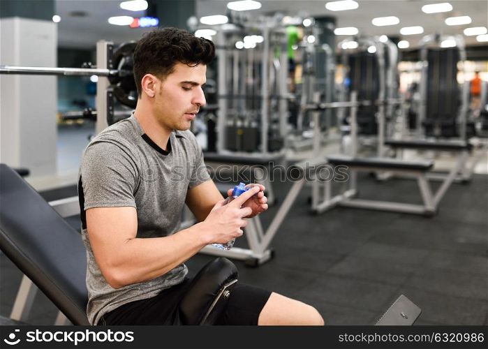 Little break. Handsome young man in sportswear holding water bottle at gym