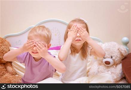Little brother and sister play in hide and seek at home, covered eyes with hands, having fun together, family relationship, happy childhood concept