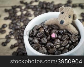 Little brown bear and coffee beans in white mug on wood background&#xA;