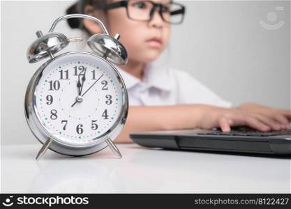 Little businesswoman with laptop working in office with vintage alarm clock on table. Children, Business and Time Concepts.