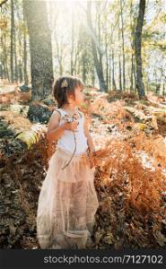 Little caucasian baby girl standing in the forest among ferns plays with plants