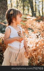 Little caucasian baby girl standing in the forest among ferns plays with plants