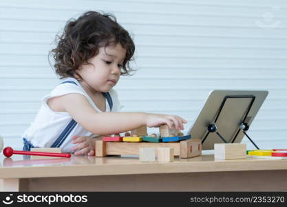 Little Caucasian kid girl playing wooden block toys and learning online on tablet at home with colorful xylophone and puzzle pieces. White background