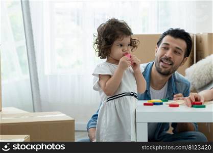 Little Caucasian kid girl trying to blow a pink balloon with puffy cheeks expression while happy young father is cheer his daughter to do it by herself. Family celebrate for move to new house together