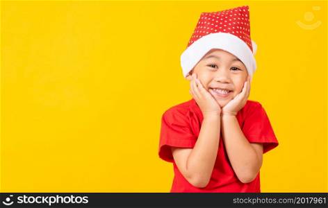 Little child boy smile and excited, Kids dressed in red Santa Claus hat shocked and surprised hand hold face concept of holiday Christmas Xmas day or Happy new year, isolated on yellow background