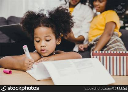 Little child girl black skin doing homework at home with sister and mother.
