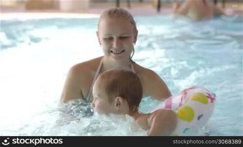 Little child having swimming lessons in a swimming pool with his mother as they laughter together and have fun splashing in the water