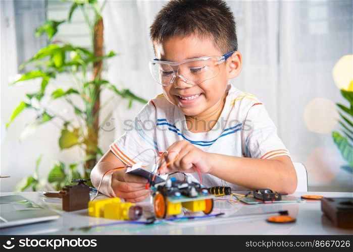 Little child remotely learn online with car toy before sent code, Asian kid boy plugging energy and signal cable to sensor chip with Arduino robot car, STEAM education AI technology course learning