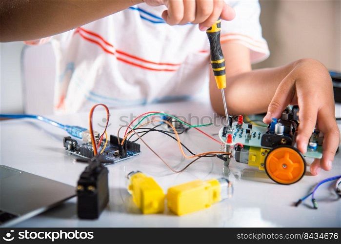 Little child tighten the nut with a screwdriver to assemble car toy, Asian kid boy assembling the Arduino robot car homework project at home, education AI technology workshop school learning lesson