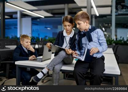 Little children coworker discussing IT project sitting on desk in modern business office. Little children coworker discussing project in office