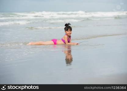 Little children girl black hair with pink, purple swimsuit running playing with sand on a beach and wave sea