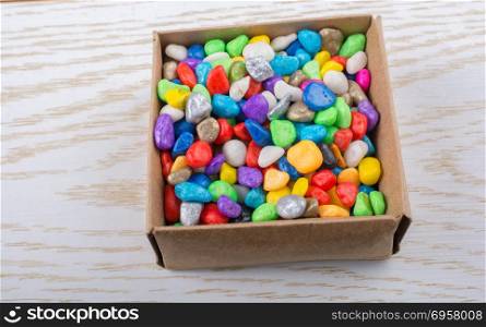 Little colorful pebbles filled in a box . Little colorful pebbles in a box on wooden texture