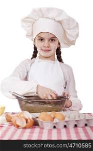 Little cook girl in a white apron breaks eggs in a deep dish, isolated on white background