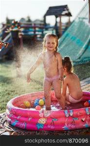 Little cute adorable girls enjoying a cool water sprayed by their father during hot summer day in backyard. Candid people, real moments, authentic situations