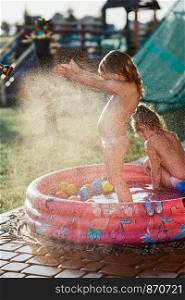 Little cute adorable girls enjoying a cool water sprayed by their father during hot summer day in backyard. Candid people, real moments, authentic situations